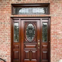 Refinished dark wood front entry door with decorative glass, set in a brick wall